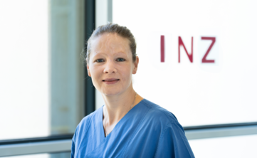 Frau mit dunkelblauen zurückgesteckten Haaren vor Glas